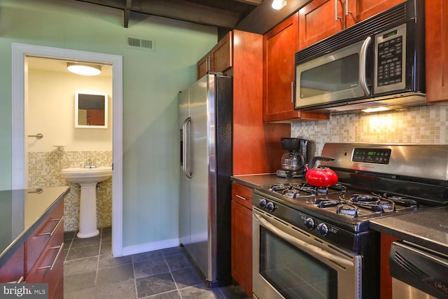 kitchen featuring stainless steel appliances, a sink, dark tile patterned floors, dark countertops, and brown cabinets