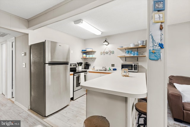 411 146th St Unit 332, Ocean City, MD 21842 - kitchen with appliances with stainless steel finishes, open shelves, a peninsula, a sink, and light wood finished floors