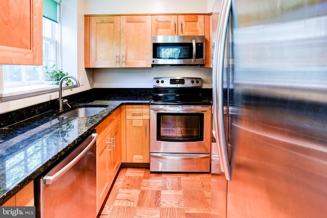 kitchen with appliances with stainless steel finishes, a sink, and dark stone countertops