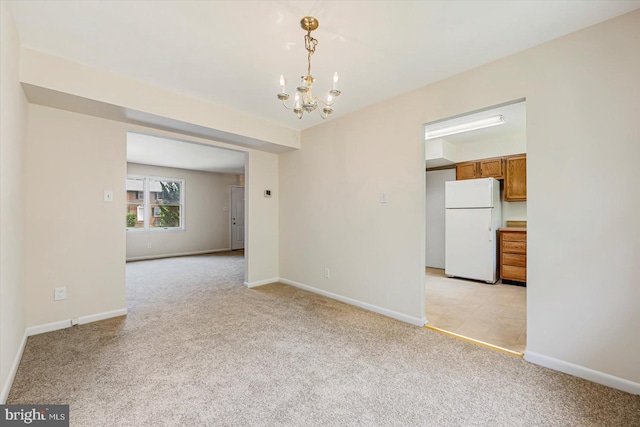 spare room featuring light colored carpet, a chandelier, and baseboards