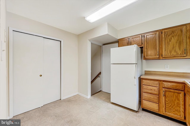 kitchen featuring freestanding refrigerator, light countertops, brown cabinetry, and light floors