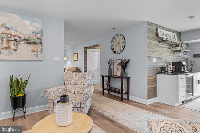 living area featuring bar with sink, light wood finished floors, wine cooler, and baseboards