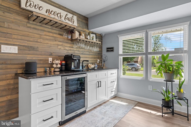 indoor wet bar with wine cooler, wood walls, baseboards, and light wood-style flooring