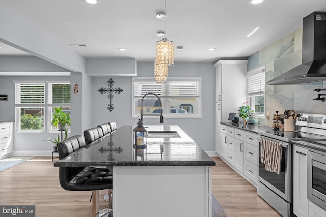 kitchen featuring wall chimney exhaust hood, appliances with stainless steel finishes, a sink, a kitchen island, and a breakfast bar area