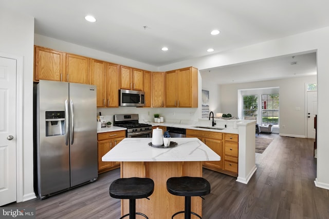 kitchen with stainless steel appliances, a sink, a peninsula, dark wood-type flooring, and recessed lighting