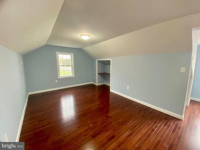bonus room with dark wood-style flooring, vaulted ceiling, baseboards, and built in shelves
