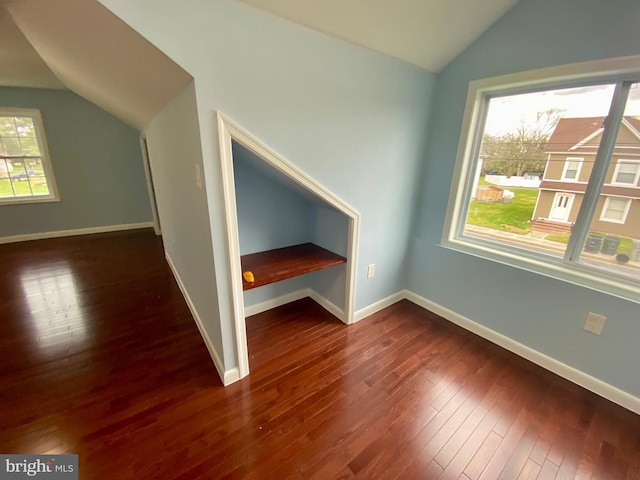 additional living space featuring lofted ceiling, plenty of natural light, dark wood-type flooring, and baseboards