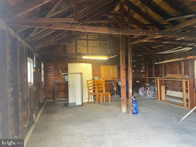 miscellaneous room with lofted ceiling, concrete flooring, and wood walls