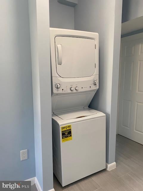 clothes washing area with stacked washing machine and dryer and baseboards