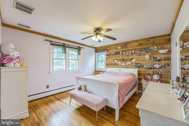 bedroom featuring a baseboard heating unit, wood walls, wood finished floors, baseboards, and a ceiling fan