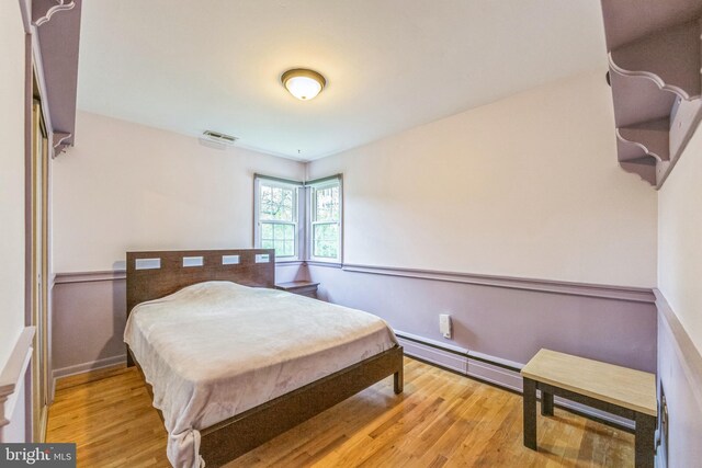 bedroom with a baseboard radiator and light wood-style flooring
