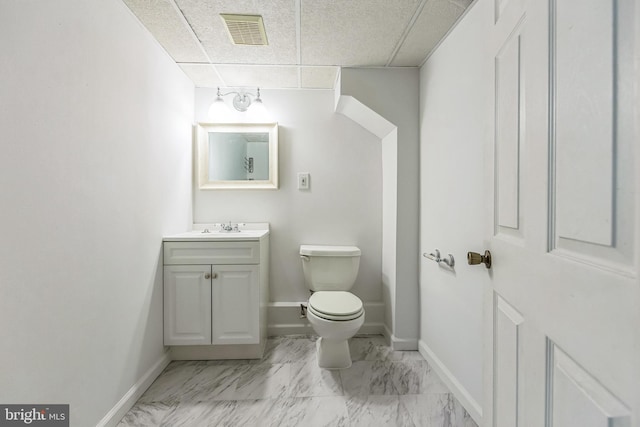 bathroom featuring a paneled ceiling, toilet, vanity, marble finish flooring, and baseboards