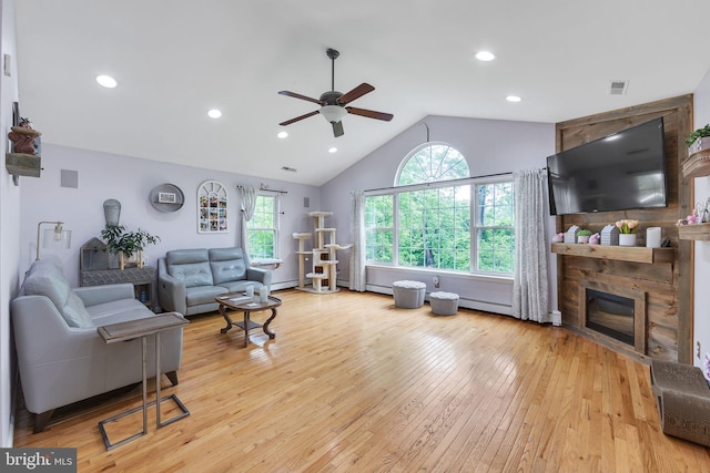 living room with ceiling fan, vaulted ceiling, hardwood / wood-style flooring, a glass covered fireplace, and a baseboard heating unit