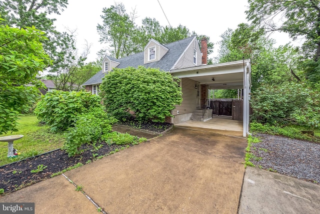 view of front facade featuring driveway, a shingled roof, a chimney, and a carport