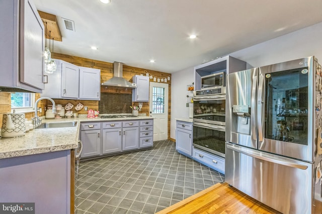 kitchen with appliances with stainless steel finishes, a sink, wall chimney exhaust hood, light countertops, and recessed lighting