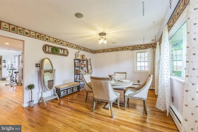 dining room featuring light wood finished floors, a chandelier, baseboards, and a baseboard heating unit
