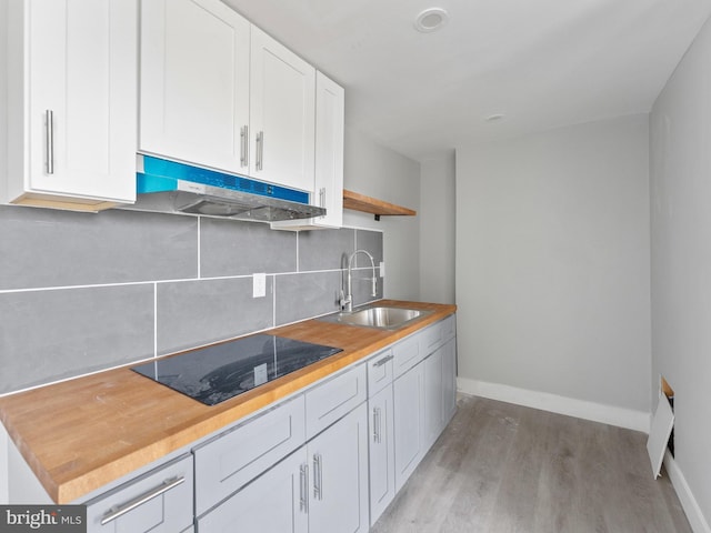 4951 W Thompson St, Philadelphia, PA 19131 - kitchen with a sink, under cabinet range hood, black electric stovetop, decorative backsplash, and white cabinets