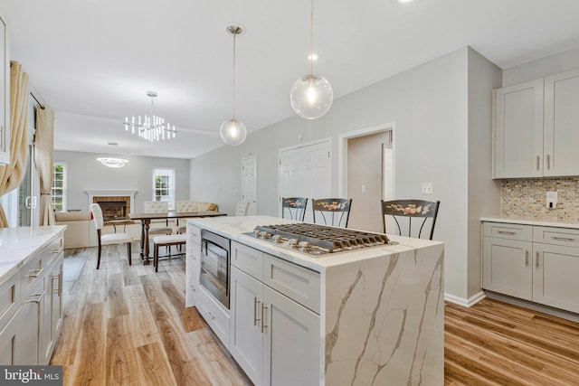 9310 Saffron Hill Ct, Manassas, VA 20110 - kitchen with stainless steel gas stovetop, black microwave, light wood-style floors, backsplash, and open floor plan