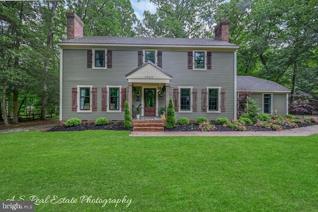 colonial-style house featuring a chimney, a front lawn, and roof with shingles