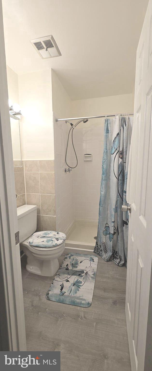 6924 Woodstream Ln, Lanham, MD 20706 - bathroom featuring toilet, wood finished floors, a shower stall, and tile walls