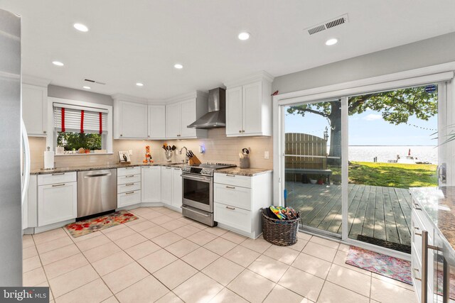 105 Bayview Ln, Hague, VA 22469 - kitchen featuring wall chimney exhaust hood, stainless steel appliances, a water view, decorative backsplash, and white cabinetry