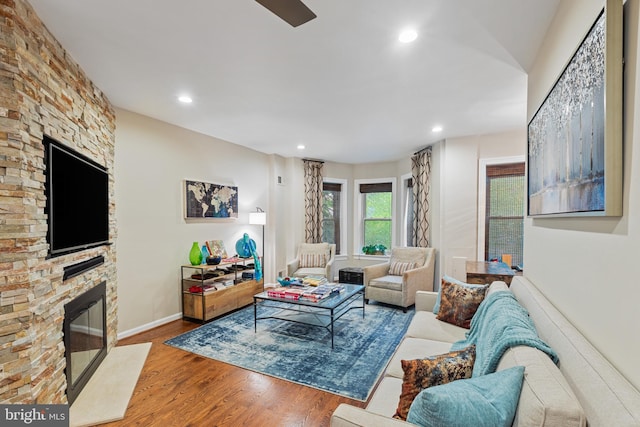 living area featuring a stone fireplace, wood finished floors, recessed lighting, and baseboards