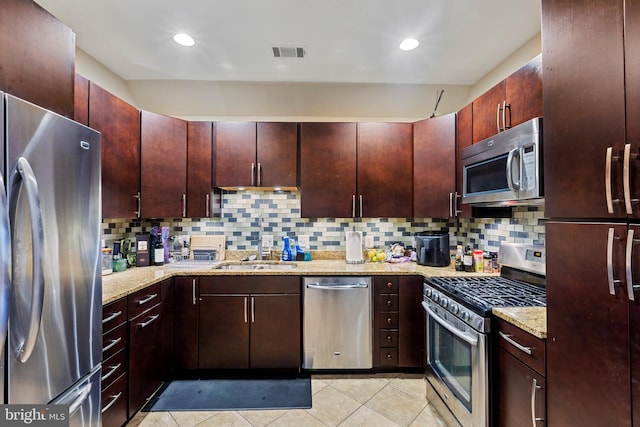 kitchen with appliances with stainless steel finishes, decorative backsplash, light tile patterned flooring, light stone countertops, and a sink