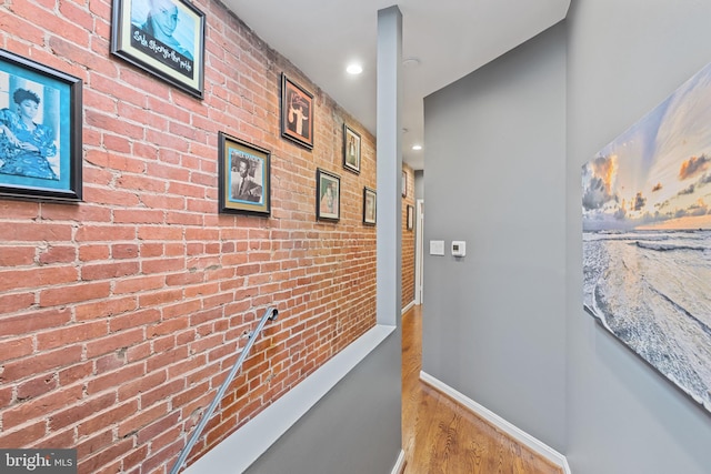 hall with wood finished floors, brick wall, baseboards, and recessed lighting
