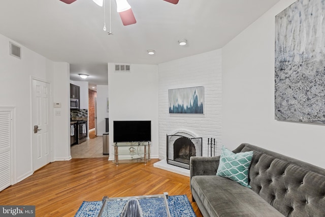 living area featuring a ceiling fan, light wood-style floors, a brick fireplace, and baseboards
