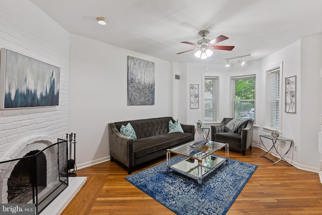 living room featuring track lighting, wood finished floors, ceiling fan, a fireplace, and baseboards
