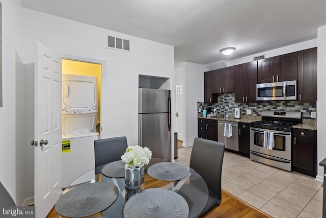 kitchen featuring appliances with stainless steel finishes, stacked washer / drying machine, tasteful backsplash, dark brown cabinetry, and a sink