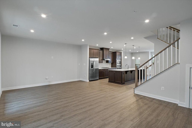 unfurnished living room featuring wood finished floors, baseboards, stairway, and recessed lighting