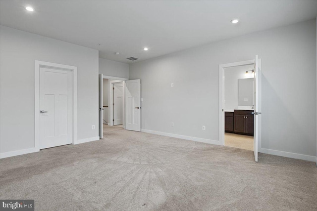 unfurnished bedroom with light colored carpet, recessed lighting, ensuite bath, and baseboards