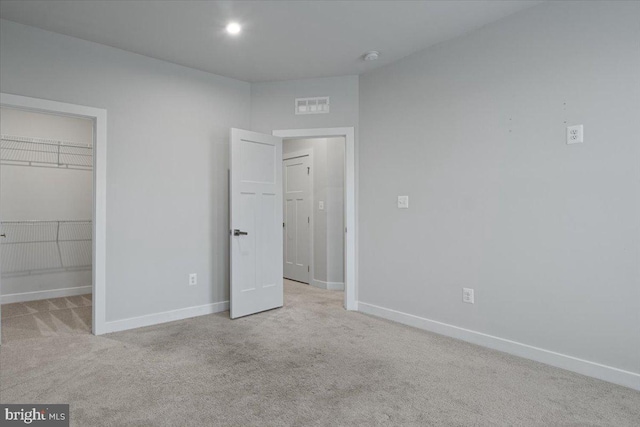 unfurnished bedroom featuring a walk in closet, carpet floors, and baseboards