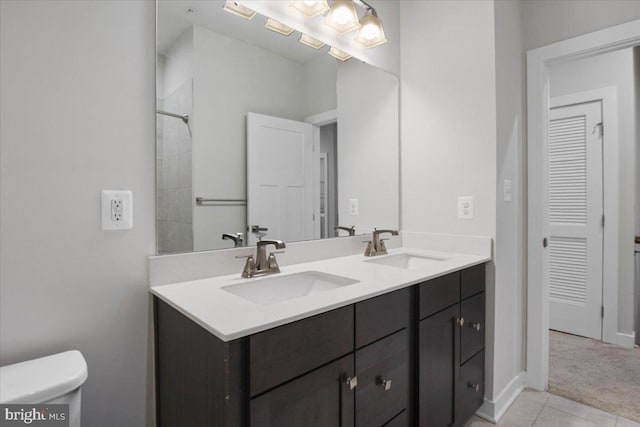 bathroom with toilet, double vanity, tile patterned floors, and baseboards