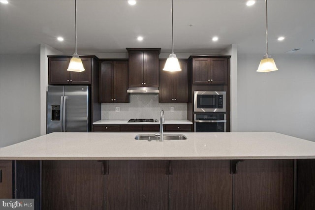 kitchen featuring stainless steel appliances, a sink, under cabinet range hood, backsplash, and dark brown cabinetry