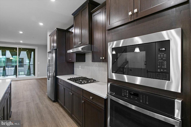 kitchen featuring stainless steel appliances, dark brown cabinets, light wood-type flooring, under cabinet range hood, and recessed lighting
