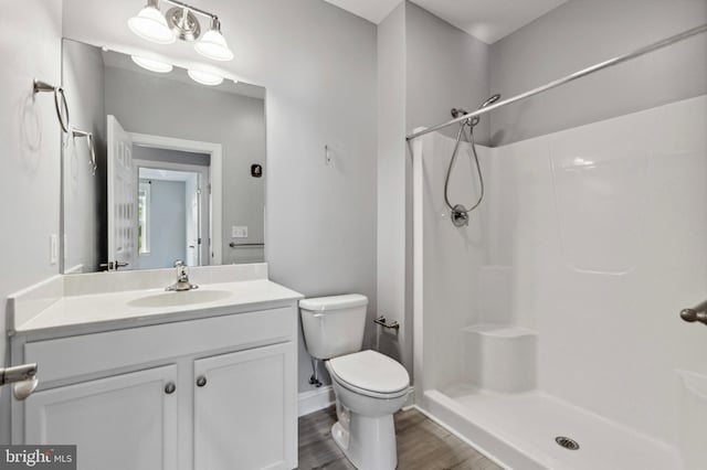full bath featuring toilet, a shower, wood finished floors, vanity, and baseboards