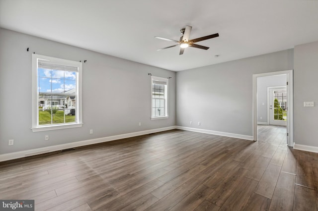 spare room with ceiling fan, healthy amount of natural light, and dark wood-type flooring