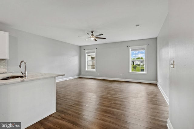 unfurnished living room with a sink, healthy amount of natural light, ceiling fan, and dark wood-style flooring