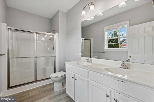 full bath with a shower stall, wood finished floors, toilet, and double vanity