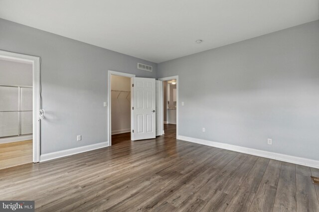 unfurnished bedroom with baseboards, dark wood-style flooring, a walk in closet, and a closet