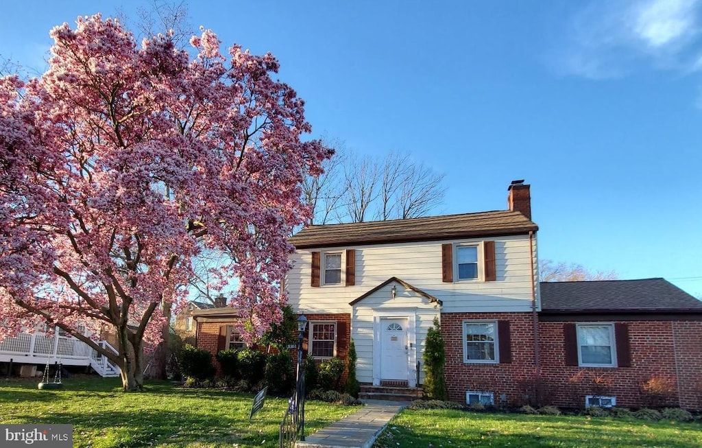 traditional-style house with brick siding, a chimney, and a front yard