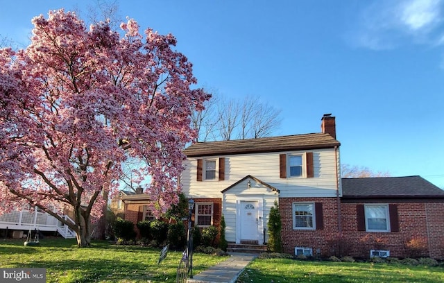 traditional-style house with brick siding, a chimney, and a front yard