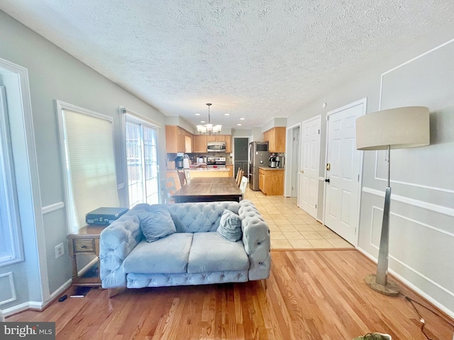 living area with a chandelier, a textured ceiling, light wood-style flooring, and baseboards