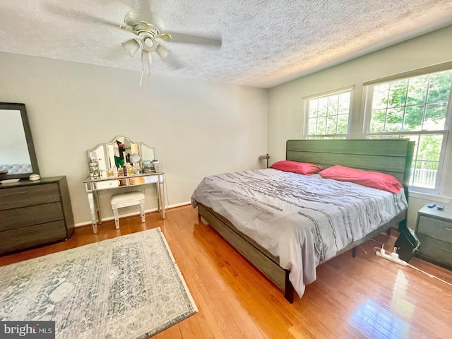 bedroom with multiple windows, wood finished floors, a textured ceiling, a ceiling fan, and baseboards