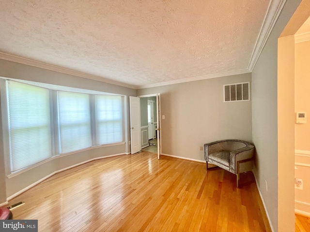 empty room featuring light wood finished floors, a textured ceiling, ornamental molding, and baseboards