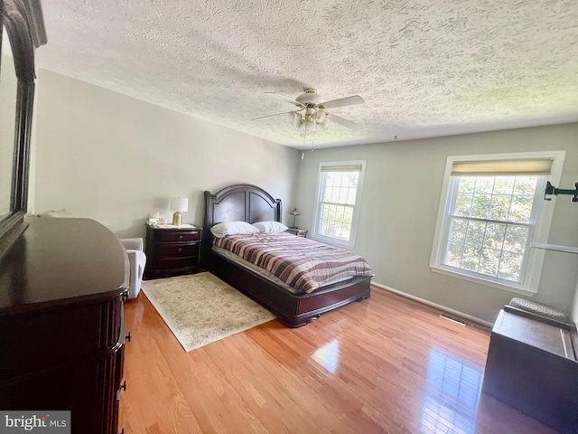 bedroom with wood finished floors, a textured ceiling, baseboards, and ceiling fan