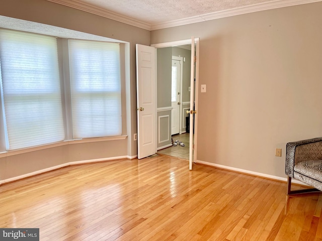spare room featuring ornamental molding, light wood-style flooring, a textured ceiling, and baseboards