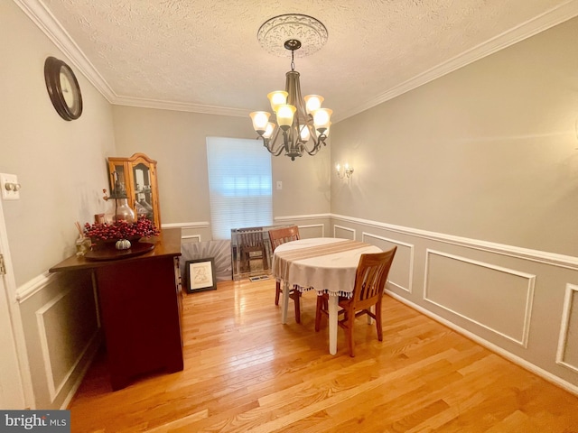 dining room with a chandelier, a textured ceiling, light wood finished floors, ornamental molding, and a decorative wall